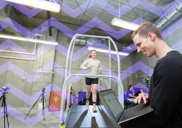 Young man working in a kinesiology lab with a person running on a treadmill. 