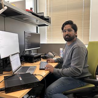 Yadhu Sivan sitting at a computer desk with three monitors and looking at the camera.