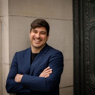 Michael MacKenzie standing against a wall and smiling at the camera.
