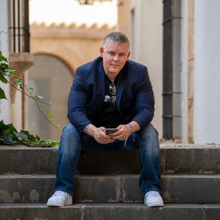 Morgan Carey sits on grey steps with an urban landscape behind him