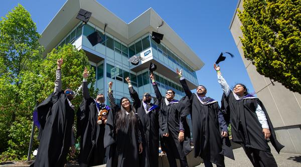students in regalia throw their grad caps in the air