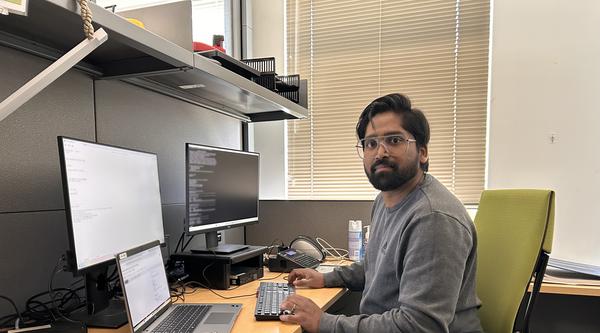 Yadhu Sivan sitting at a computer desk with three monitors and looking at the camera.