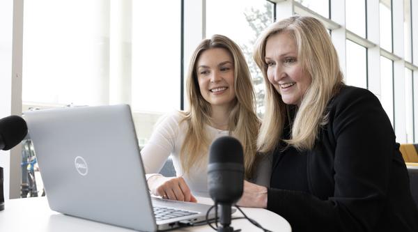 Two women look at a computer screen together with a microphone next them