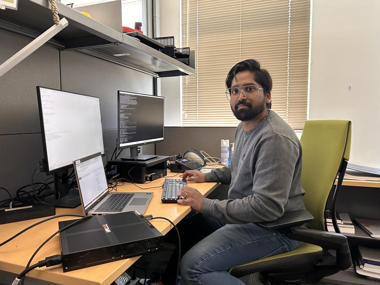 Yadhu Sivan sitting at a computer desk with three monitors and looking at the camera.