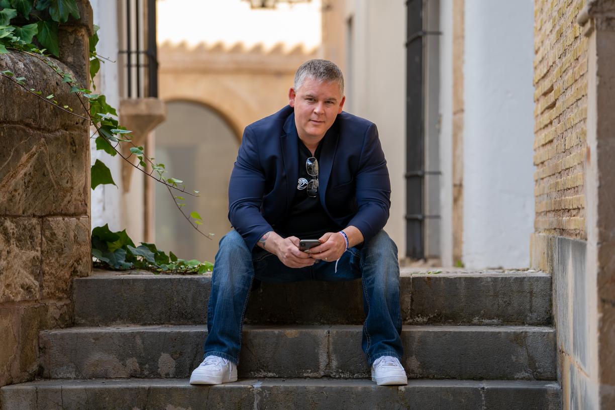 Morgan Carey sits on grey steps with an urban landscape behind him